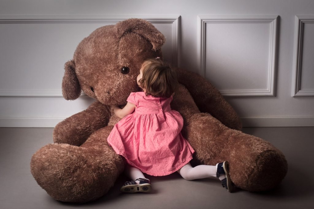 A small girl kisses a giant bear. 