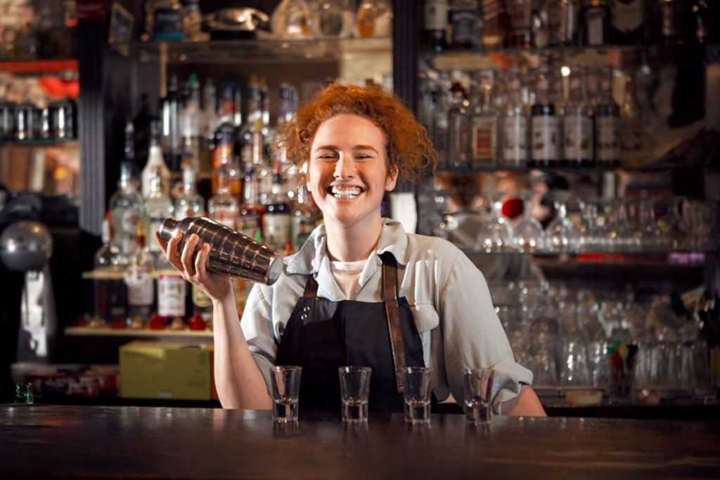 A female bartender laughs as she mixes a drink. 