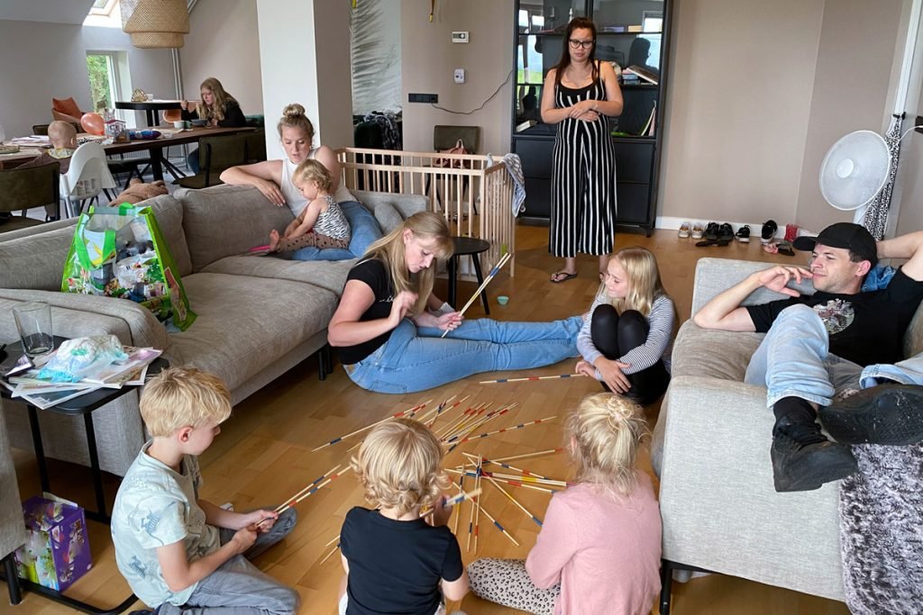 A large family play a game of pick up sticks in their living room. 