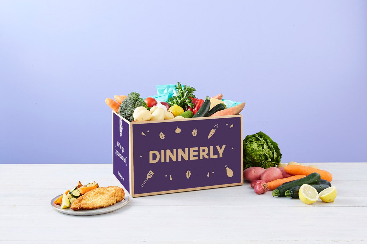 Food and vegetables sit outside of a Dinnerly box. 
