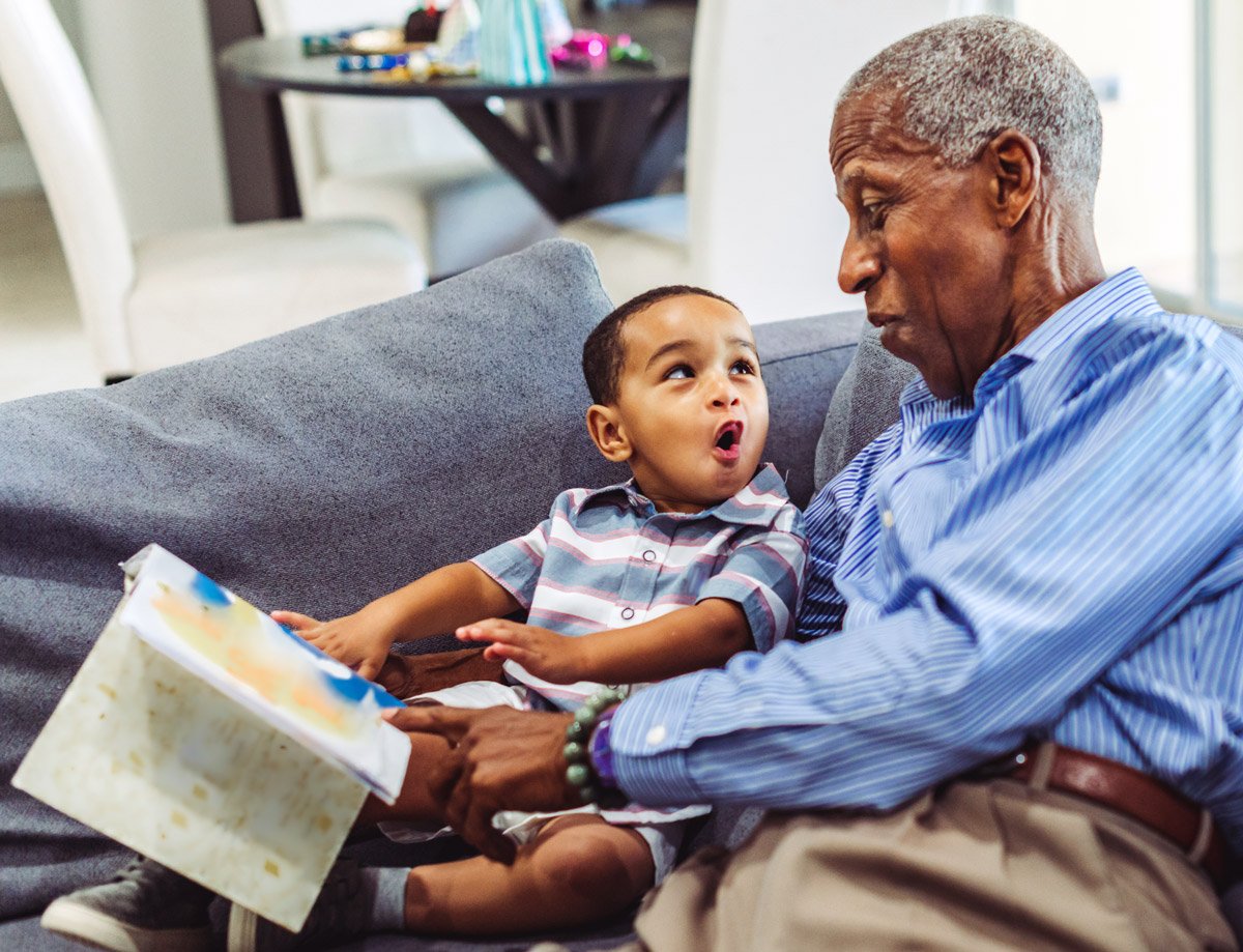 A grandfather and grandson react while reading a book on a couch. 