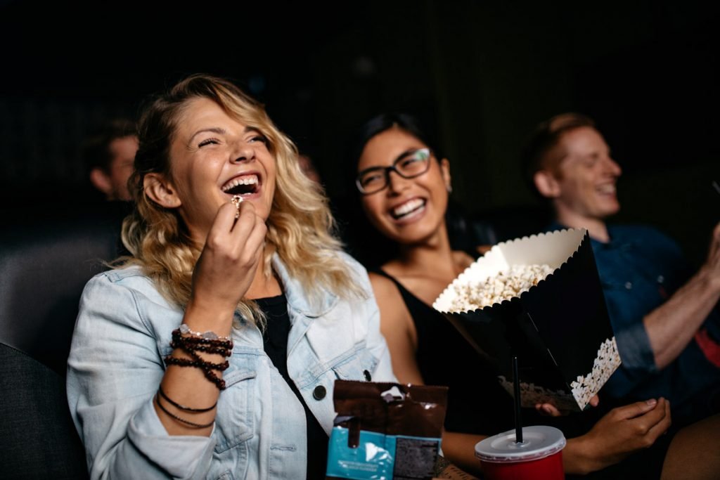 Two people laugh while watching a movie at the movie theater. 