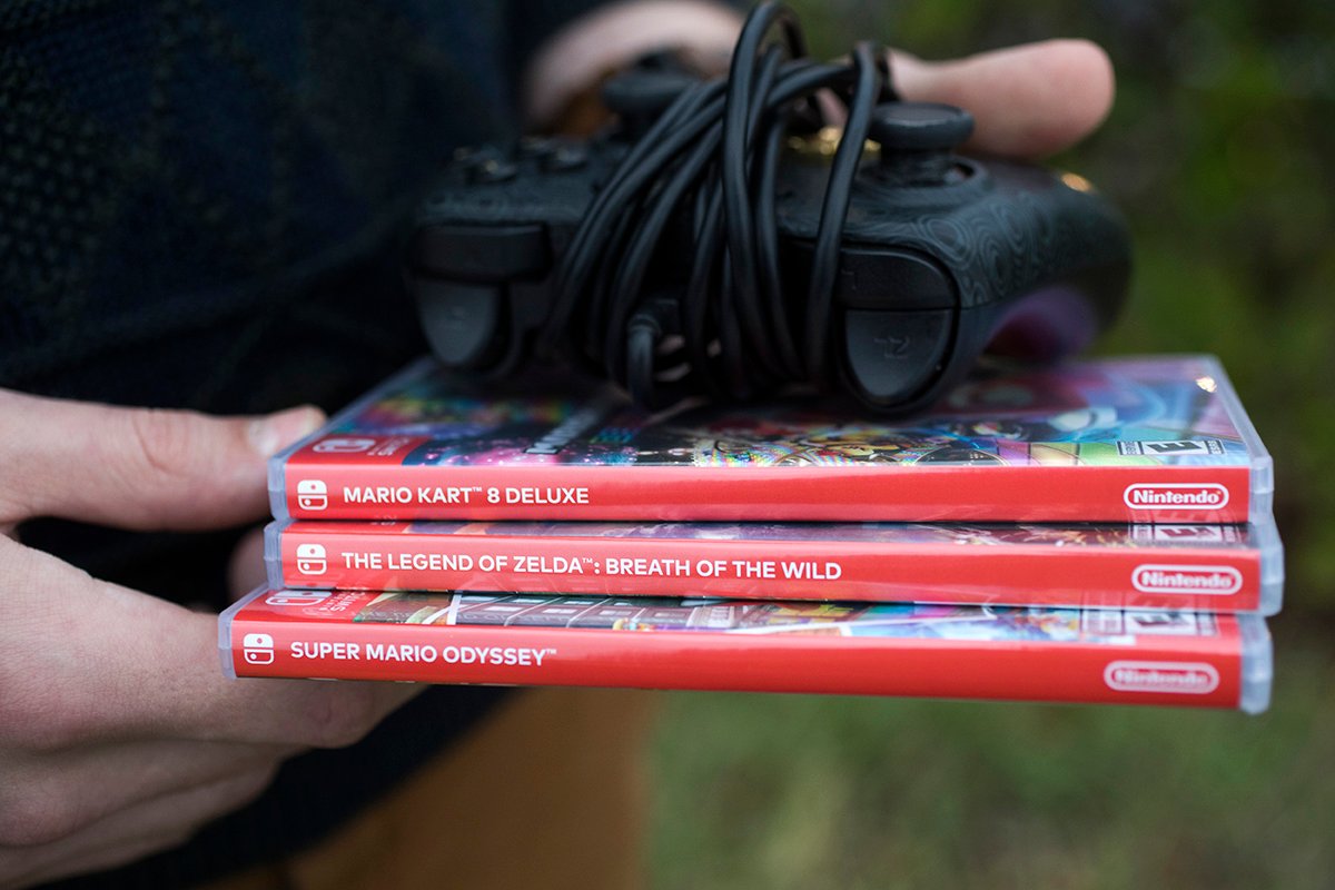 A person holds video game boxes and a controller.