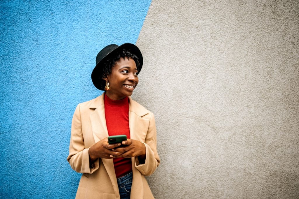 A trendy woman smiles with a phone in her hand. 