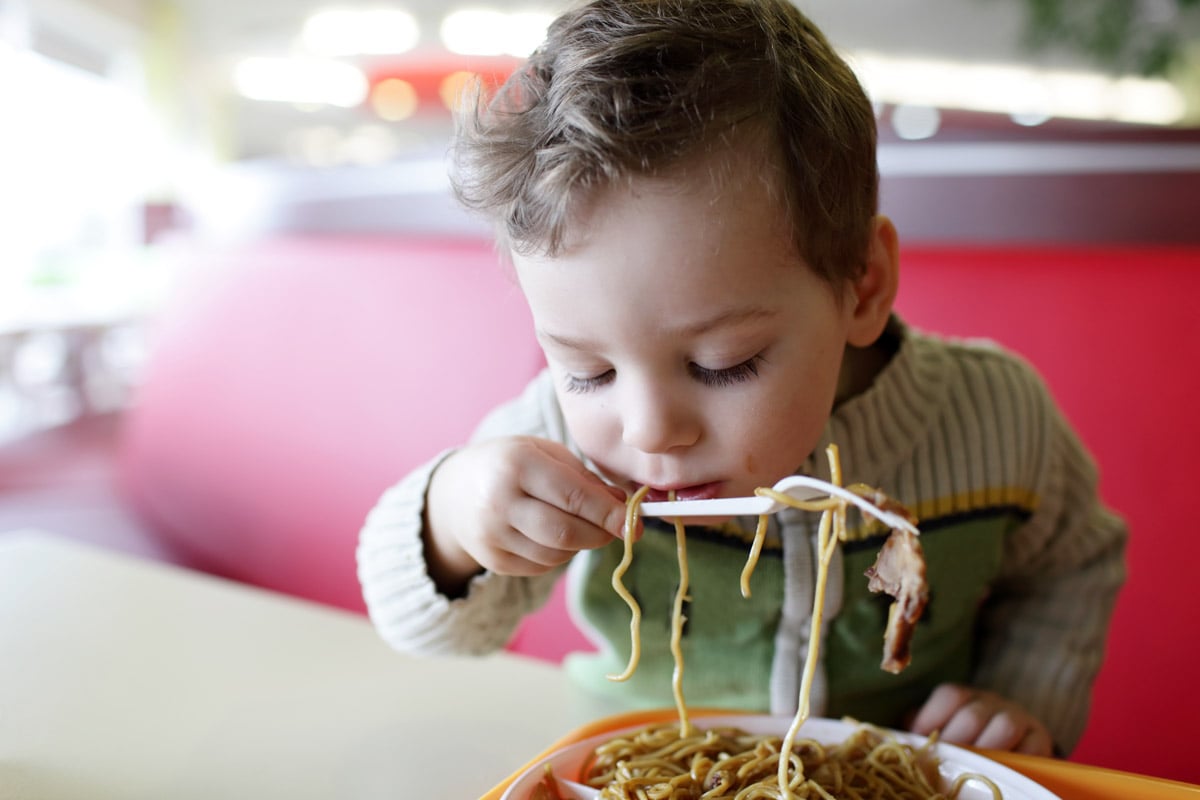 A little boy eats pasta.