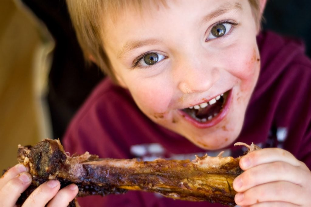 A boy eats a rack of ribs. 