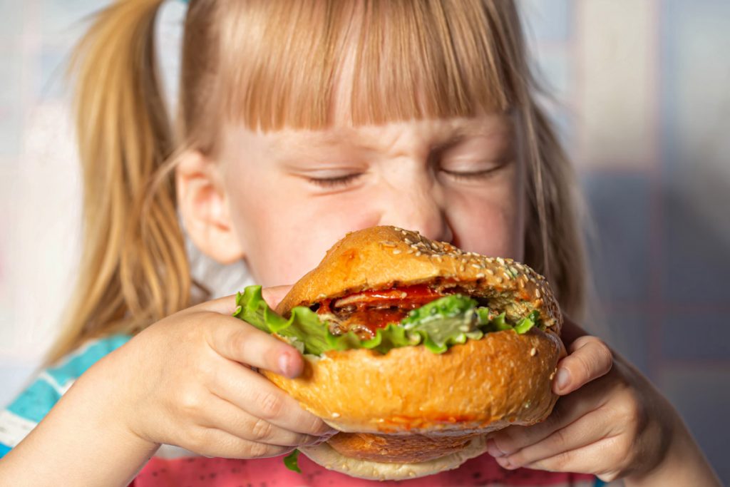 A little girl eats a hamburger. 