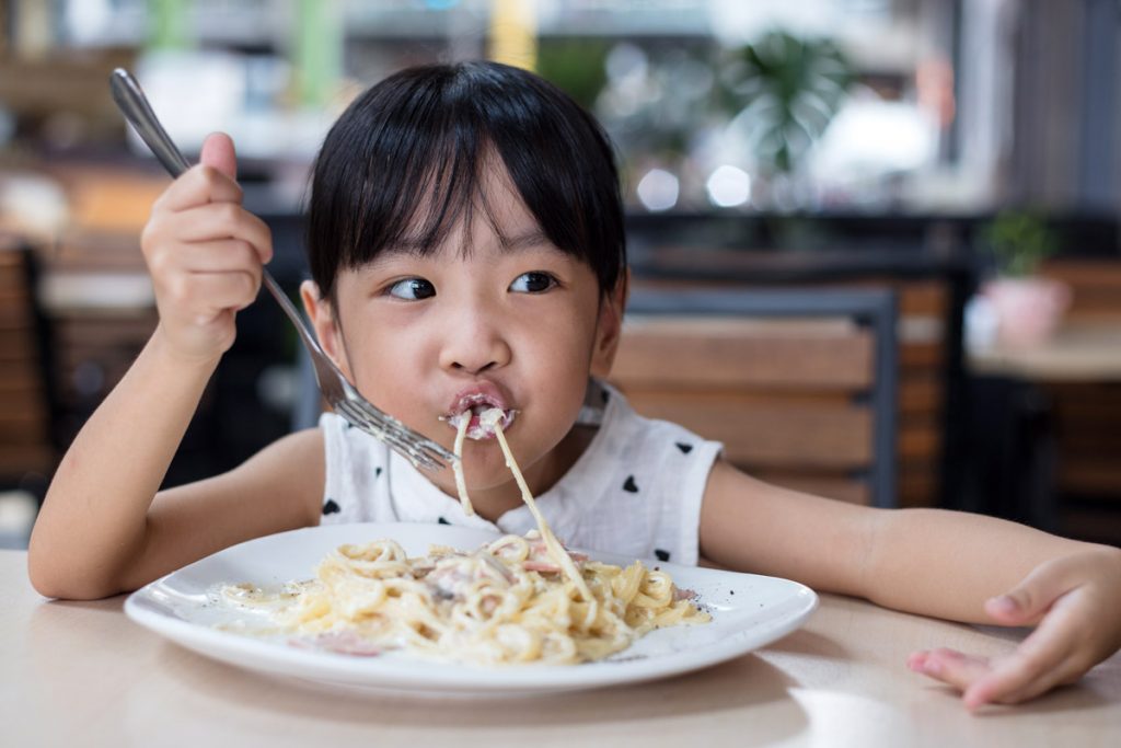 A little girl eats pasta at a restaurant. 