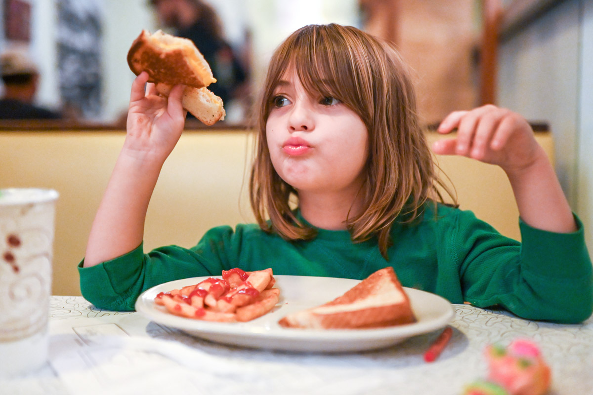 A little girl eats grilled cheese and fries.