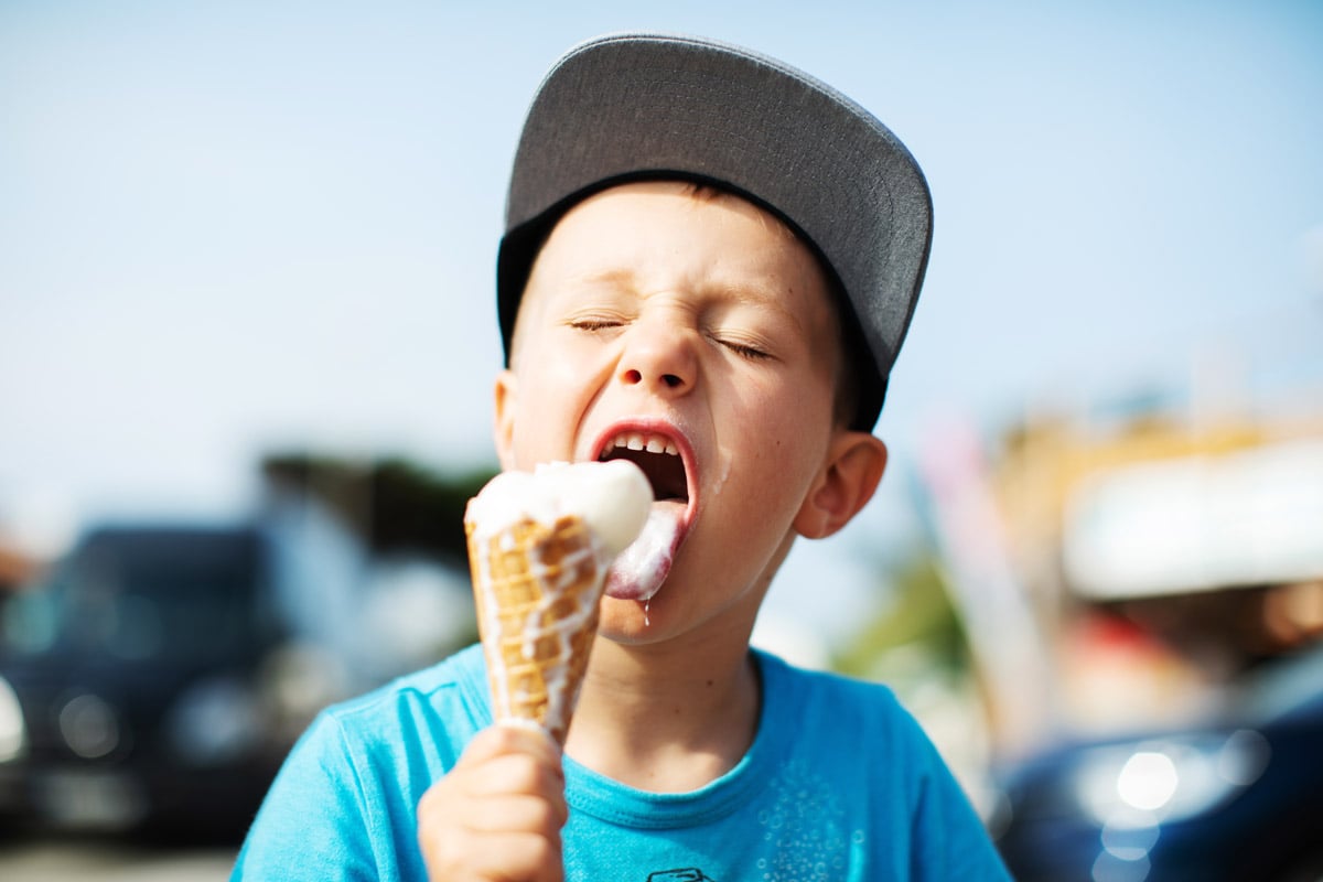 A little boy eats ice cream outside.
