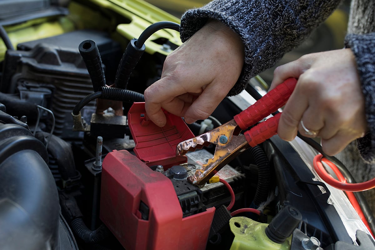 A woman uses jumper cables to start up a yellow Honda fit.
