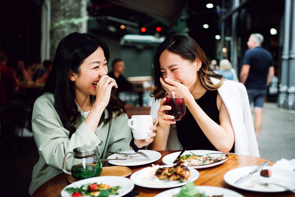 Two friends laugh as they enjoy dinner at a restaurant.