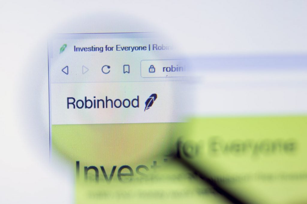 A magnifying glass is shown taking a closer look at the word Robinhood on a computer. They are in a class action lawsuit due to a data breach.