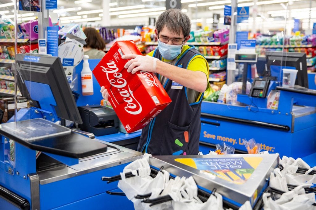 A man rings up a pack of coca-cola for a customer at Walmart. 