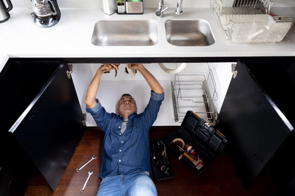 A man fixes a leaky pipe underneath a sink. 