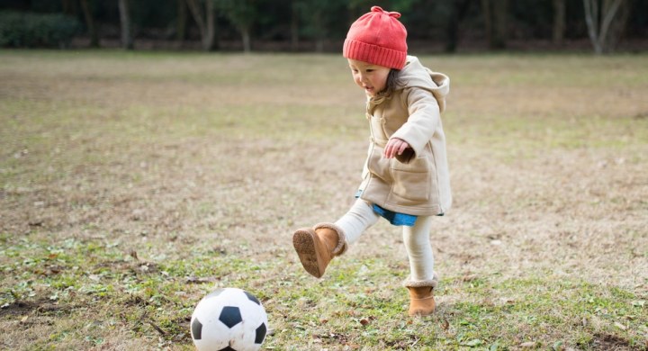 Little girl playing football on frosty grass