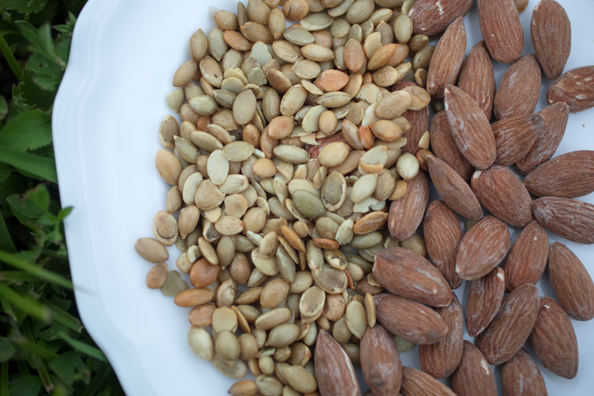 Pumpkin seeds and almonds sit in a white bowl.